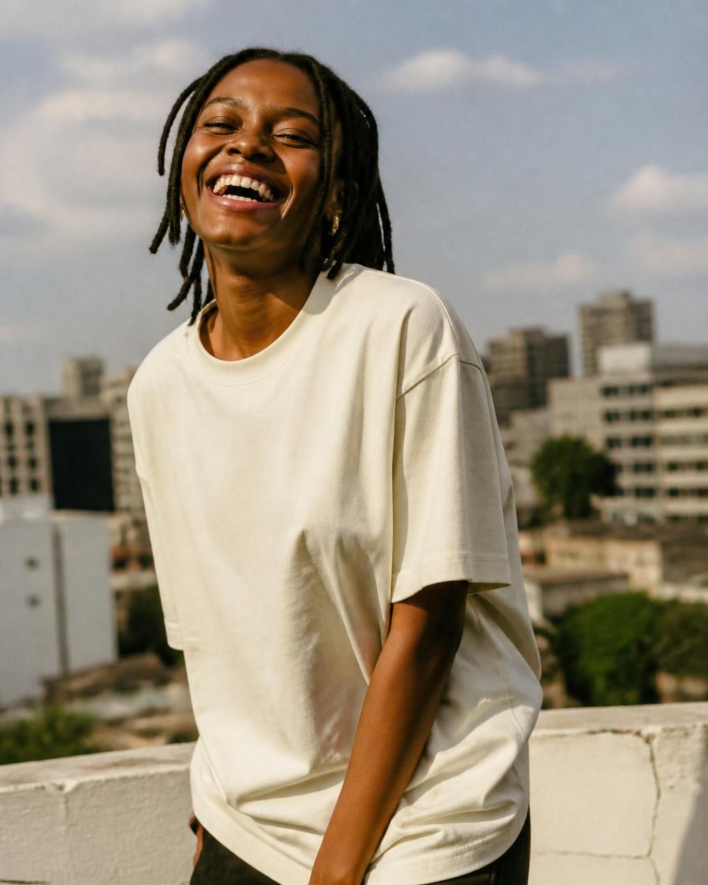 Woman laughing on a sunlit Nairobi rooftop in an oversized cream T-shirt