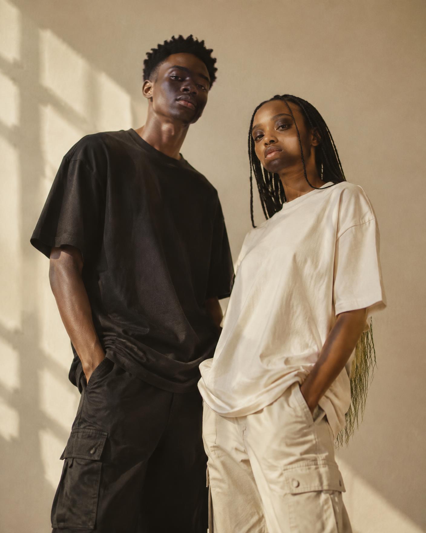Two people wearing black and cream oversized tees in warm daylight